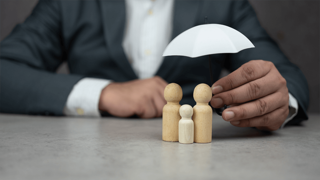 Person holding an umbrella over wooden figures of a family unit - symbolizing protecting your business during a divorce.