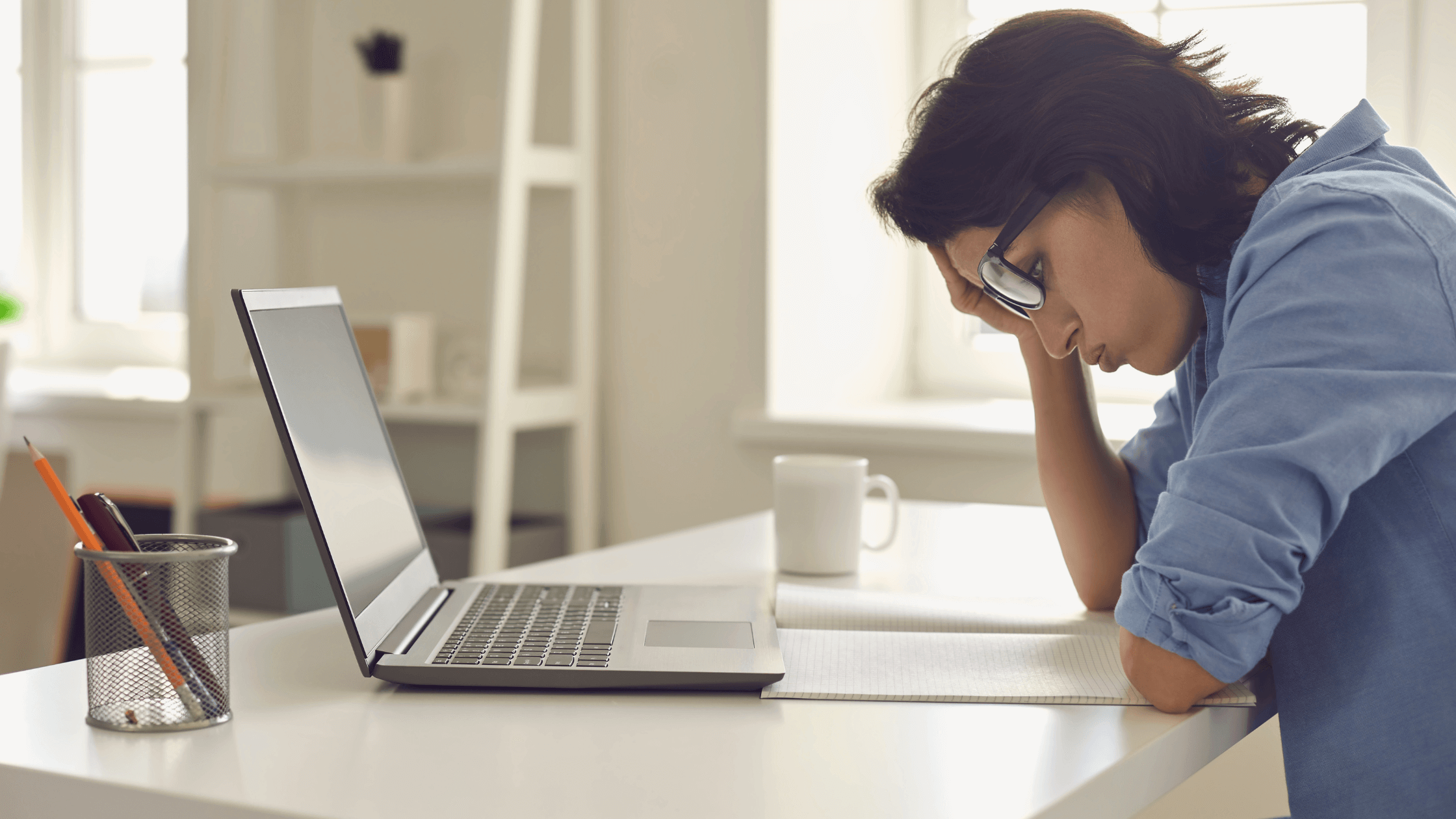 Woman looking stressed while working on a laptop, resting her head on her hand.