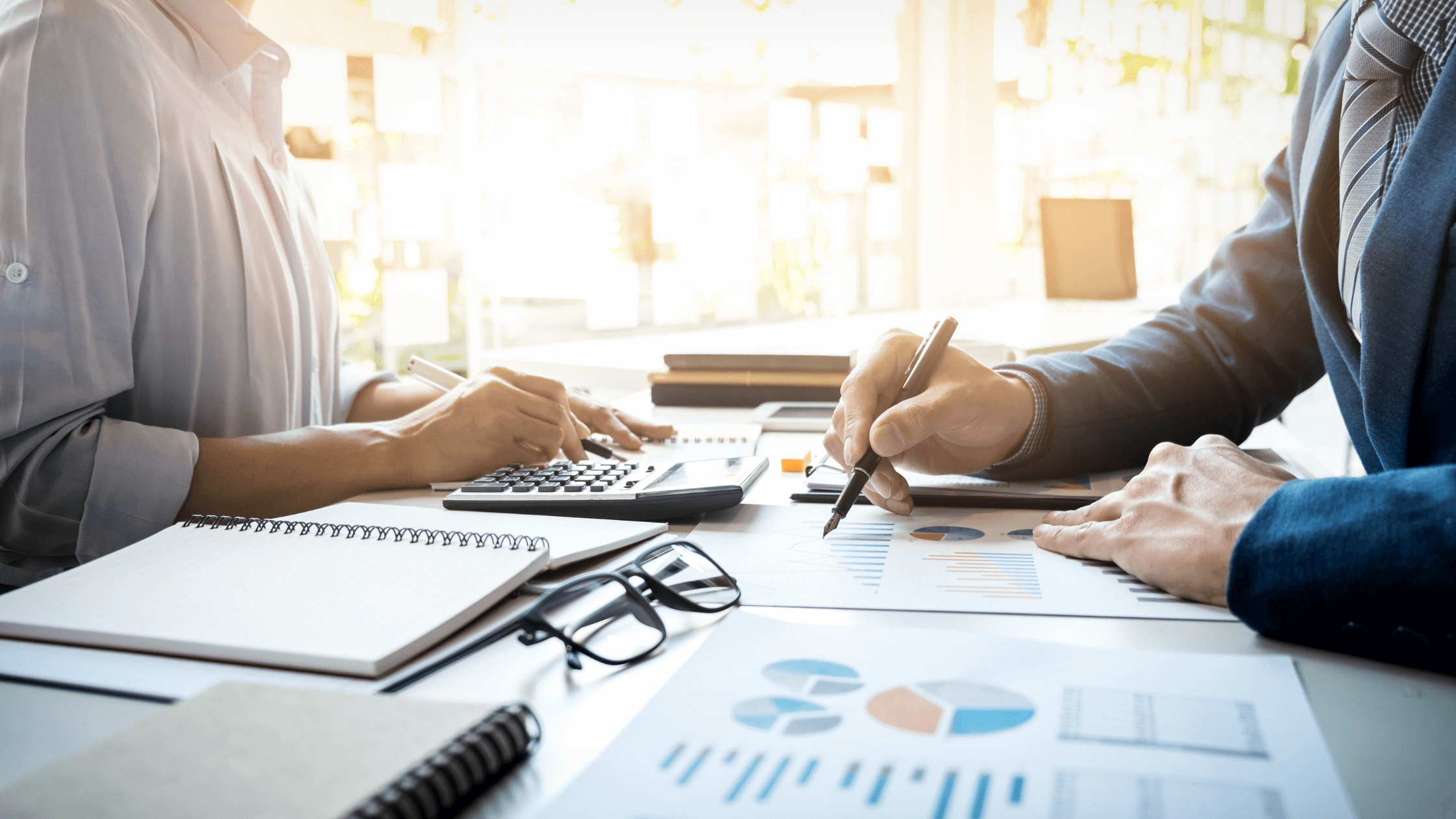 A lawyer and client sit at a desk, using a calculator and reviewing financial charts.
