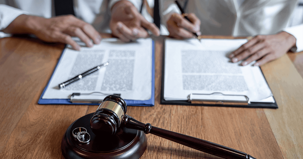 An overhead shot of a laptop keyboard, a gold pen, a small desk calendar pinned with a thumbtack, and an alarm clock, symbolizing the strategic timing and planning involved in filing for divorce.