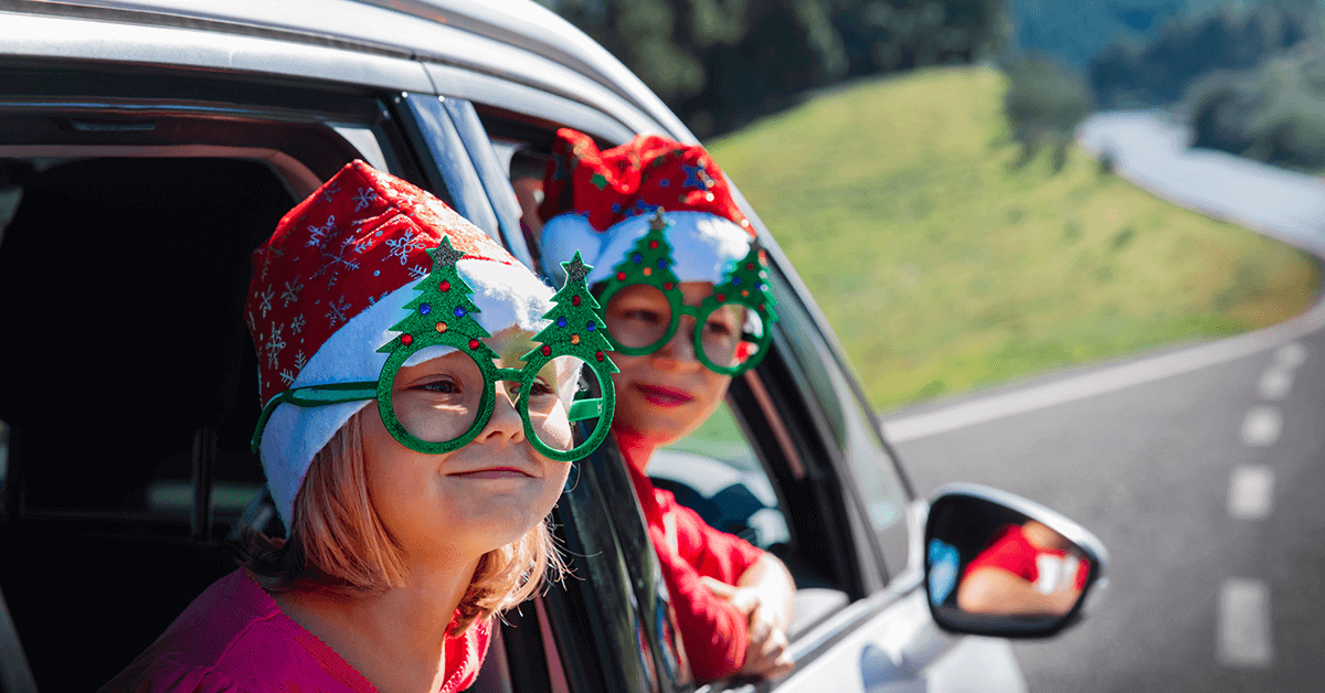 Two young, excited children, a boy and a girl, sitting by a Christmas tree opening a red present, symbolizing the joy of the holiday season shared by siblings.