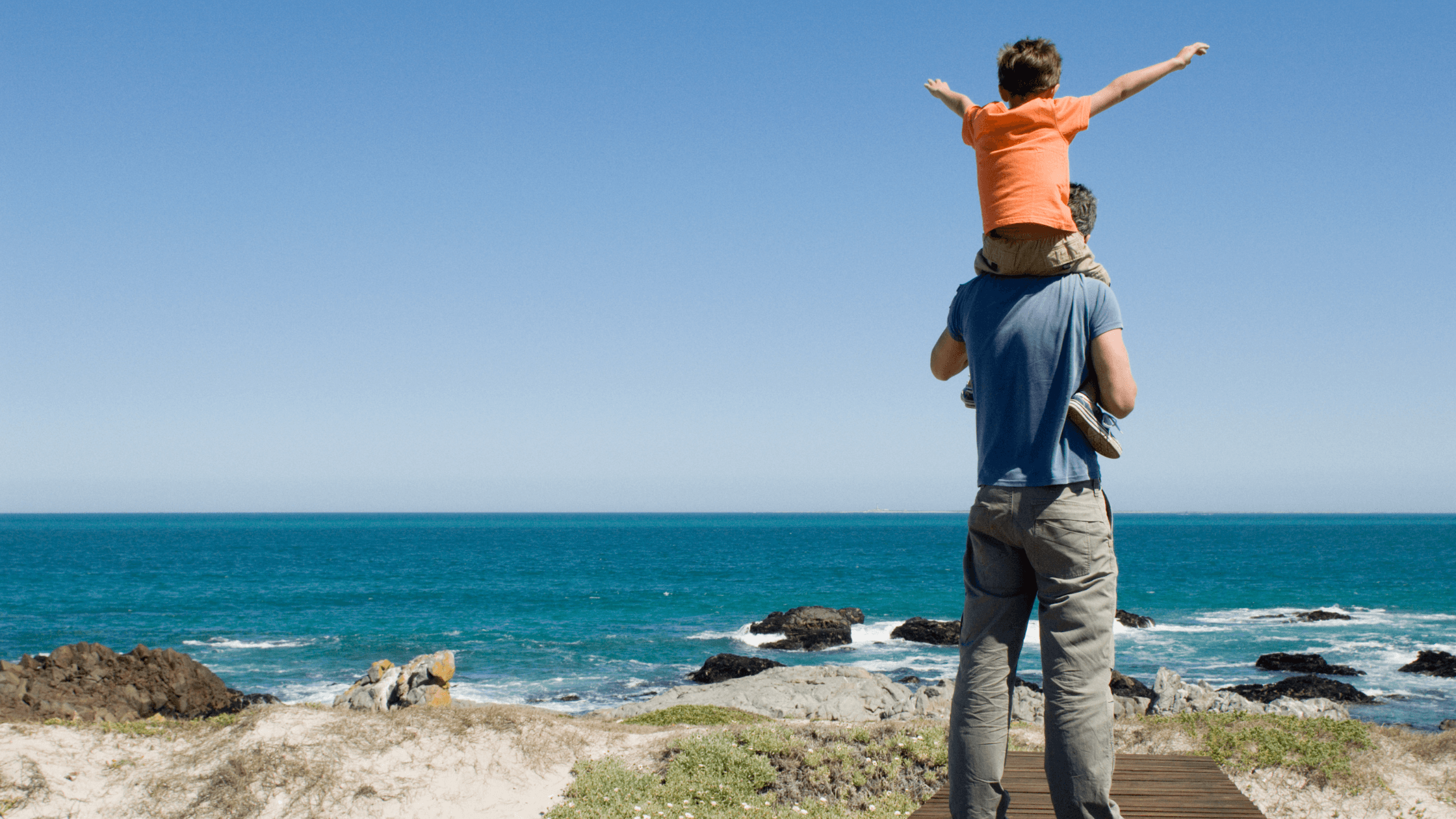 A father holding his young son on his shoulders while looking out at the ocean, illustrating the importance of Father's Day visitation rights in Texas.