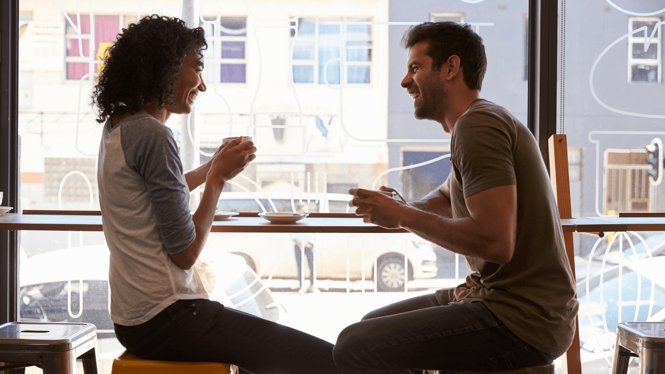 A man and woman sitting at a cafe window and laughing over coffee, representing the complexities of dating while a Texas divorce is still pending.